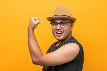 Vaccinated asian funny man showing arm after coronavirus Vaccination isolated yellow Background. Indian man getting a vaccination covid-19 immunization