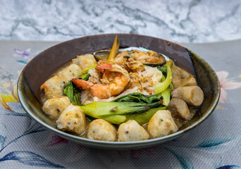 Thin rice noodles soup with mussels, shrimp, meatball, mushroom and vegetable serving in ceramic bowl. Asian style food, Selective focus.