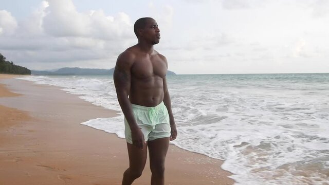 African American man walks on the beach at sunset. shorts and nude top