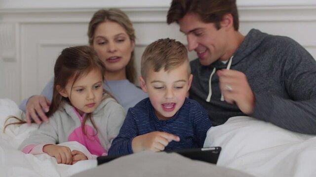 happy family using tablet computer at bedtime mother and father with children watching entertainment playing game on touchscreen device learning having fun together at home 4k footage 