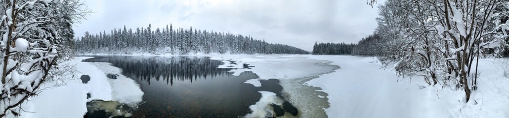 Giant panorama of snow-covered ice-river among a frozen taiga forest in a winter