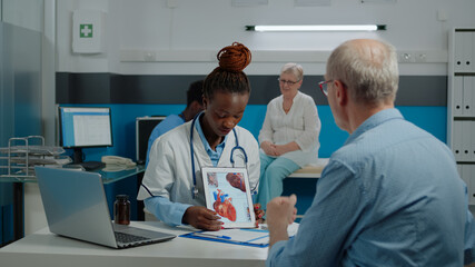 Obraz premium Woman cardiologist holding modern tablet with cardiovascular system, explaining heart disease to elder caucasian patient looking at device, sitting in hospital room at facility