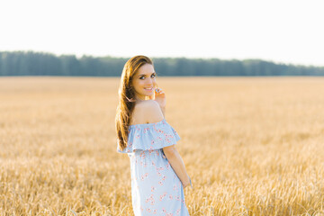 Fototapeta na wymiar A young woman in a blue dress stands in a field of rye at sunset