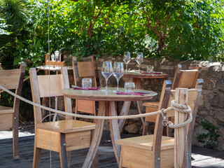 Fototapeta na wymiar Empty Wooden Tables with Crystal Wine tasting Glasses Set for Outdoor Lunch in a Tuscan Village in Italy