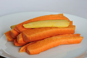 Orange carrots and white carrots sticks on a white plate, white background