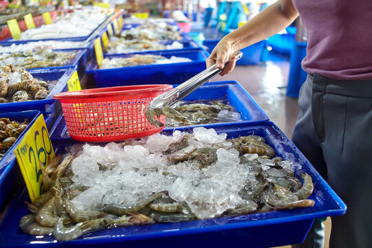 human hand holding silver tong for picking fresh chrimp at seafood market