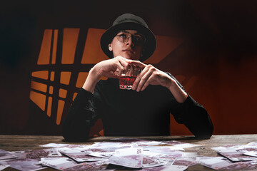 A cool man in dark glasses at a table with money and alcohol