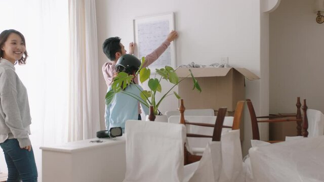 happy asian family moving into new home owners hanging picture decorating house together with children young couple enjoying real estate property investment with kids 4k footage