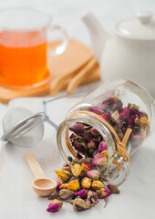 Rose buds mix tea with wooden scoop and strainer infuser on white with ceramic teapot and clear cup.