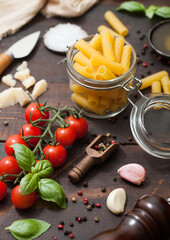 Fresh raw penne pasta in glass jar with tomatoes and basil, garlic and oil with parmesan cheese and salt and pepper on wooden background.