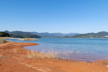The lake under the blue sky has blue water and red land