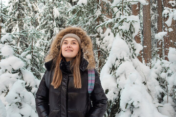 young woman in a winter down jacket with fur hood walks in the forest in winter