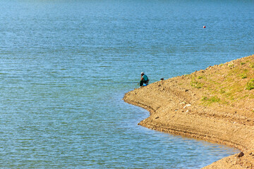 Lonely fisherman on the beach, in blue water background. Copy space