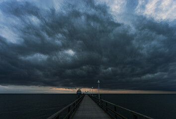 Pier leading to the sea with a dark cloudy sky over it - Powered by Adobe