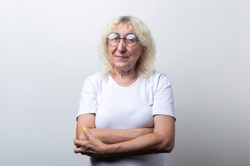 Smiling old woman in a white T-shirt with glasses on a light background.