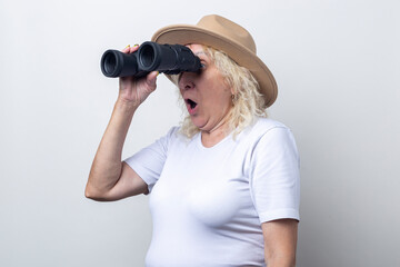 Surprised old woman holding binoculars on a light background