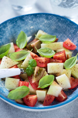 Close-up of salad with melon, red tomatoes and fresh green basil leaves served in a blue bowl, vertical shot, selective focus