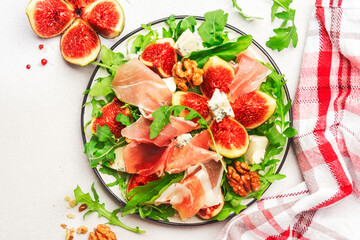 Sweet fig salad with jamon, blue cheese, walnuts, arugula on white background, top view, copy space