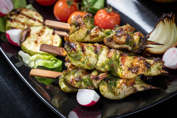 Grilled turkey skewers, skewered on wooden skewers, in a large plate decorated with herbs, zucchini and tomatoes.