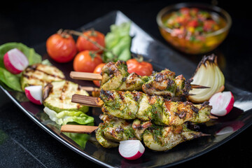 Grilled turkey skewers, skewered on wooden skewers, in a large plate decorated with herbs, zucchini and tomatoes.