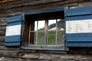 Fototapeta na wymiar Reflection of mountains in the window of an old wooden house. Austria