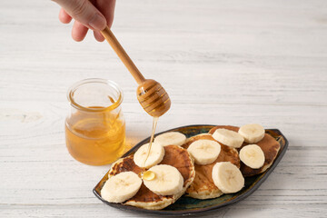 Homemade pancakes on a white wooden table. Drop of honey pouring on top of banana pancakes