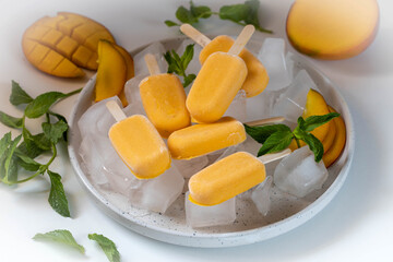 Ice cream sorbet from mango and banana. Ice cream on a stick in a large plate with ice cubes,...
