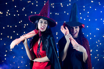 Studio shot of Asian and Caucasian scary fierce sexy female models in black red witch dress costume tall hat and shawl look at camera holding fake cut arms organ with blood in Halloween festive party