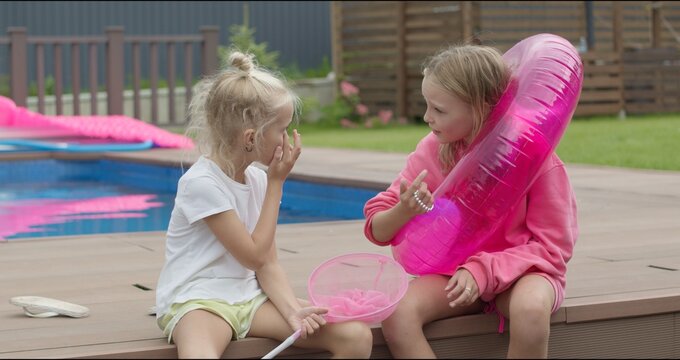 Portrait of happy sisters sitting near swimming pool