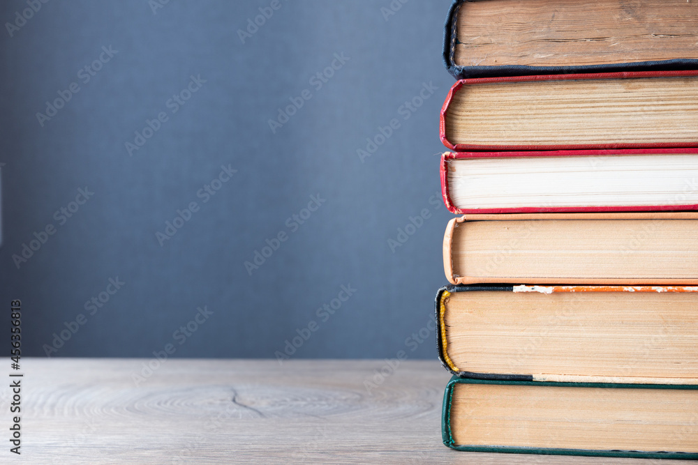 Poster stack of old books on wooden table and gray background with copy-space to left. background concept o