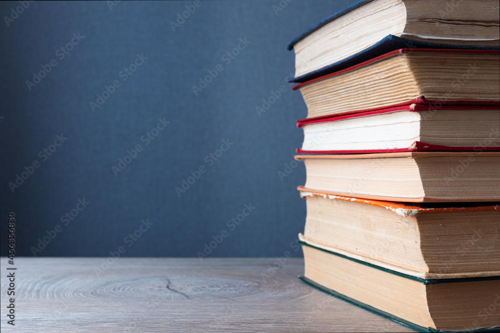 Poster stack of old books on wooden table and gray background with copy-space to left. background concept o
