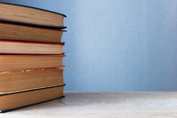 stack of old books on wooden table and gray background with copy-space to right. Background concept on education, knowledge, usefulness of reading and self-development.