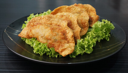 handmade deep fried and boiled pork meat dumpling wanton soup in plate on dark grey wood table...