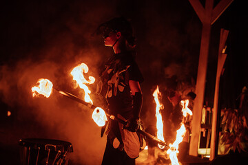 a fireshow artist in a mask of a mythical creature performs with fire. street culture festival. colorful mystical fire show at night