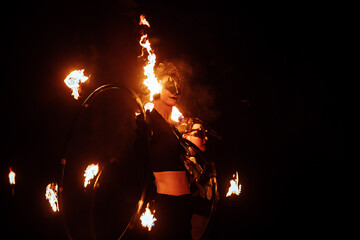 Fototapeta na wymiar a fireshow artist in a mask of a mythical creature performs with fire. street culture festival. colorful mystical fire show at night
