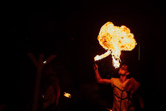 the fireshow artist exhales fire. a dangerous and beautiful performance of the street art theater. the fire tamer spits flames. the fire eater in the circus