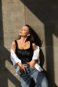 Pretty Young Woman With Big Breast Posing In Studio, By Steel Wall On Background, Wearing Jeans And White Shirt, Natural Warm Sunset Light