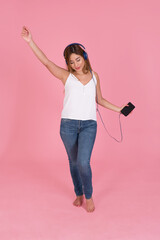Latin woman listening to modern music, with wired headphones dancing on pink background