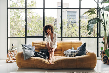 Young and beautiful african american woman sitting on a couch looking at camera in a bright loft apartment