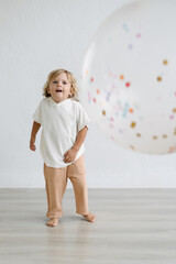 Three years old blonde caucasian kid playing with a big confetti balloon in a white background