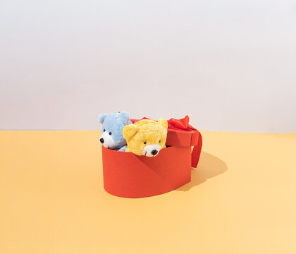 Red gift box from which yellow and blue teddy bears come out on silver and gold background. Minimal arrangement.