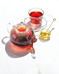 Fruit tea with apples and thyme and honey in glass teapot and cup on white background with hard shadows