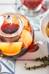 Fruit tea with apples and thyme in glass teapot and cup on table made of colored tiles