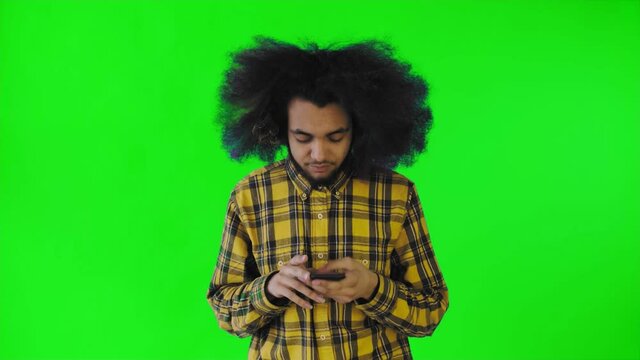 A young man with an African hairstyle on a green background pulls out his phone, but it doesn't work. Emotions on a colored background