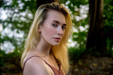 Fototapeta premium Portrait of a young blonde girl on the background of the park.