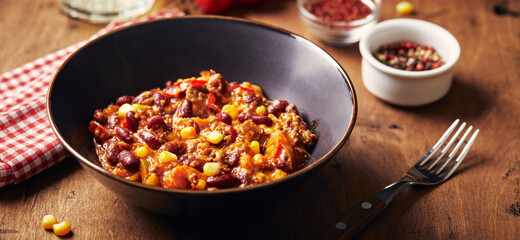 Chili Con Carne with ground beef, beans and corn in dark bowl on wooden background. Mexican and...