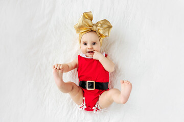 Funny little Santa. Cute baby girl in a red Santa Claus costume on bed. Merry Christmas.