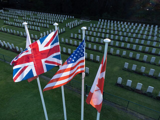 Flags flapping in the wind by war graves at Schoonselhof cemetery graveyard in Wilrijk Antwerp Belgium Union Jack, US Canada