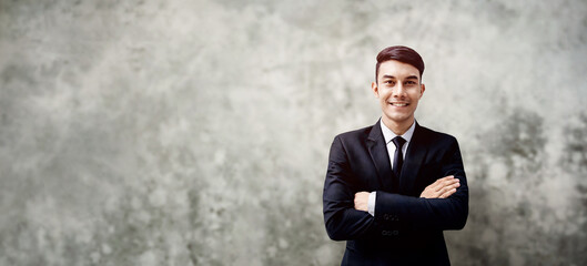 Smiling Young Businessman Standing by the Loft Concrete Wall. Crossed Arms and Looking at Camera. more copy space with Wide size