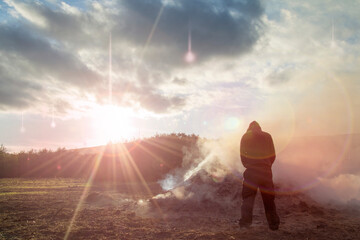 A ufo concept. Of a hooded figure, back to camera, looking at a debris smoking, As glowing lights, with light trails fall from the sky. With light flare.